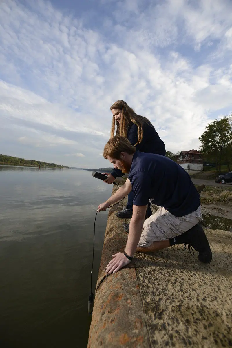Students on the edge of the Biology Field Station dock gather river water samples for research and monitoring.