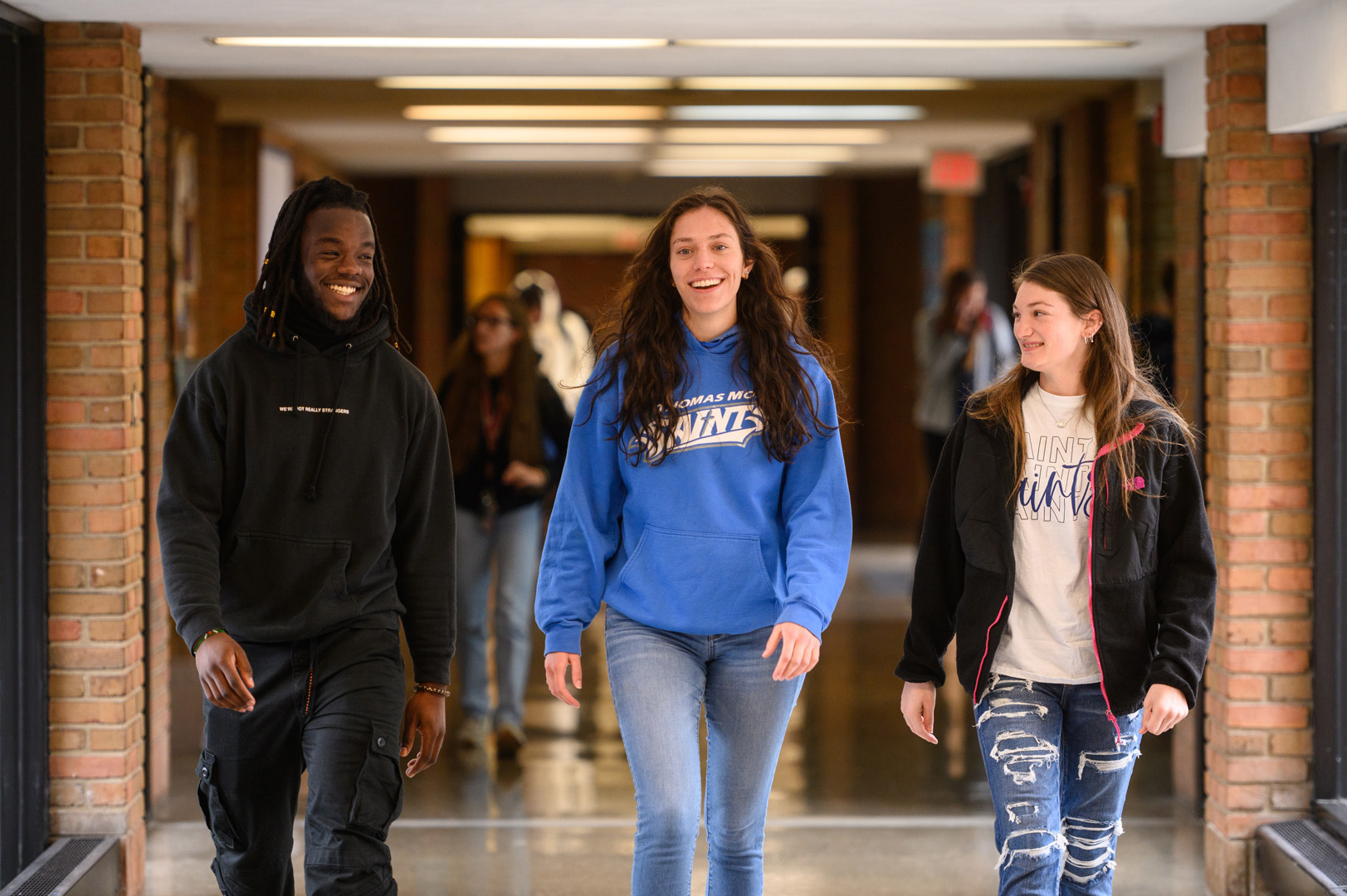 Three students interact as they walk down interior hallway