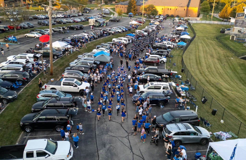 The cheer, dance, and football teams walking with the marching band through the Homecoming tailgate towards Republic Bank Field.