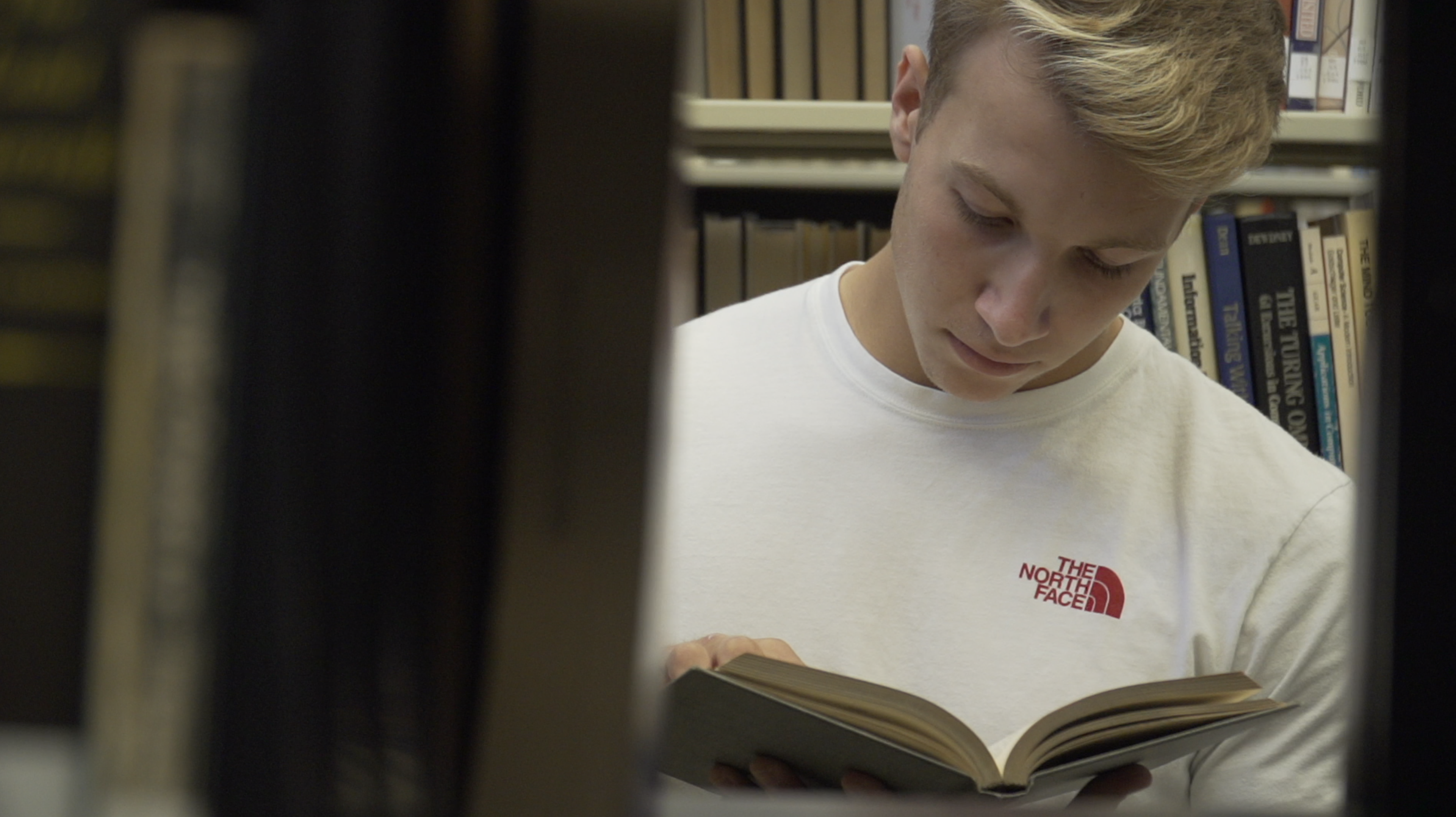 Student reads a book in the library in preparation for class.