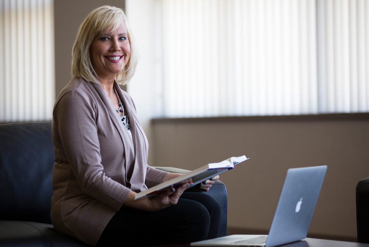 woman holding book in front of lap top